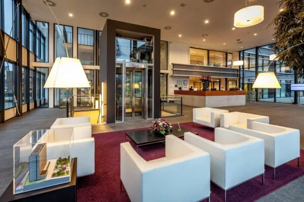 Moderne ontvangsthal aan de Prinses Beatrixlaan met witte zithoeken, een lift, balie en maquette van een gebouw.